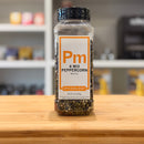 Bottle of Pm 4 Mix Peppercorn Whole on a wooden surface with a blurred kitchen background.