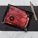 Raw beef steak on a black slate board with a knife on a marble surface