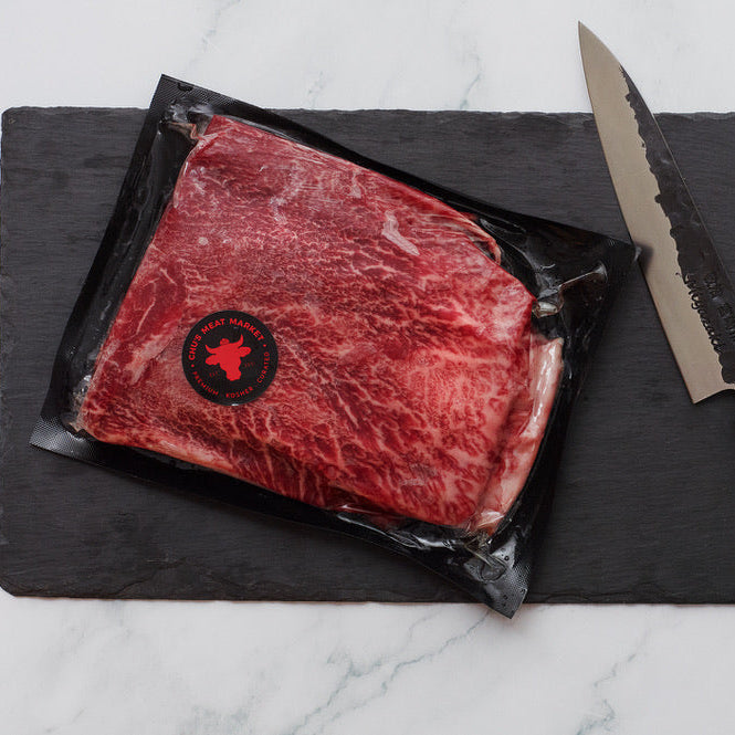 Raw beef steak on a black slate board with a knife on a marble surface