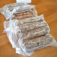 Gourmet kosher wagyu beef sausages, cryovaced a sitting on a wood countertop. ."