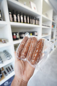 Hand holding a vacuum-sealed package of frozen kosher wagyu beef sausages at Chu's Meat Market.