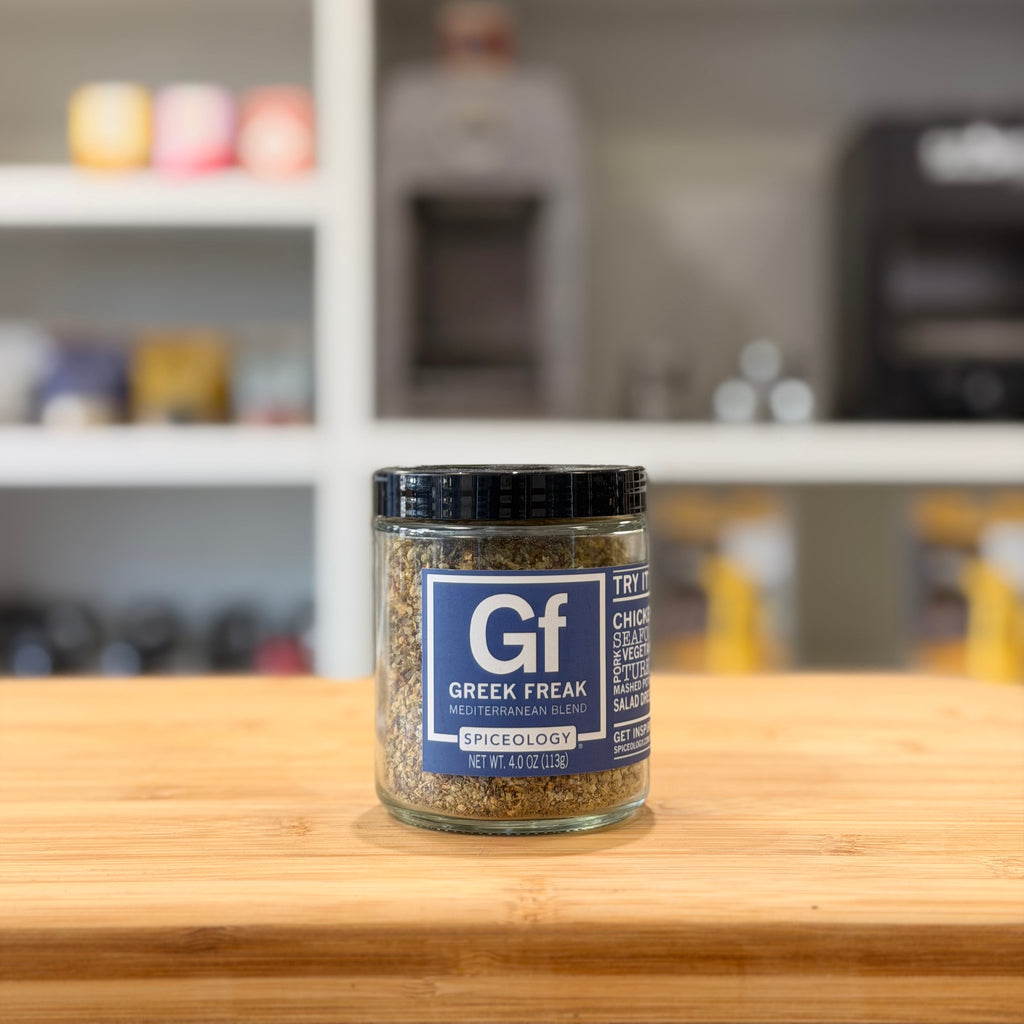 Jar of Gf Greek Freak spice mix on a wooden surface with a blurred kitchen background