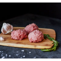Three raw meatballs on a wooden cutting board with garlic and rosemary on a dark surface