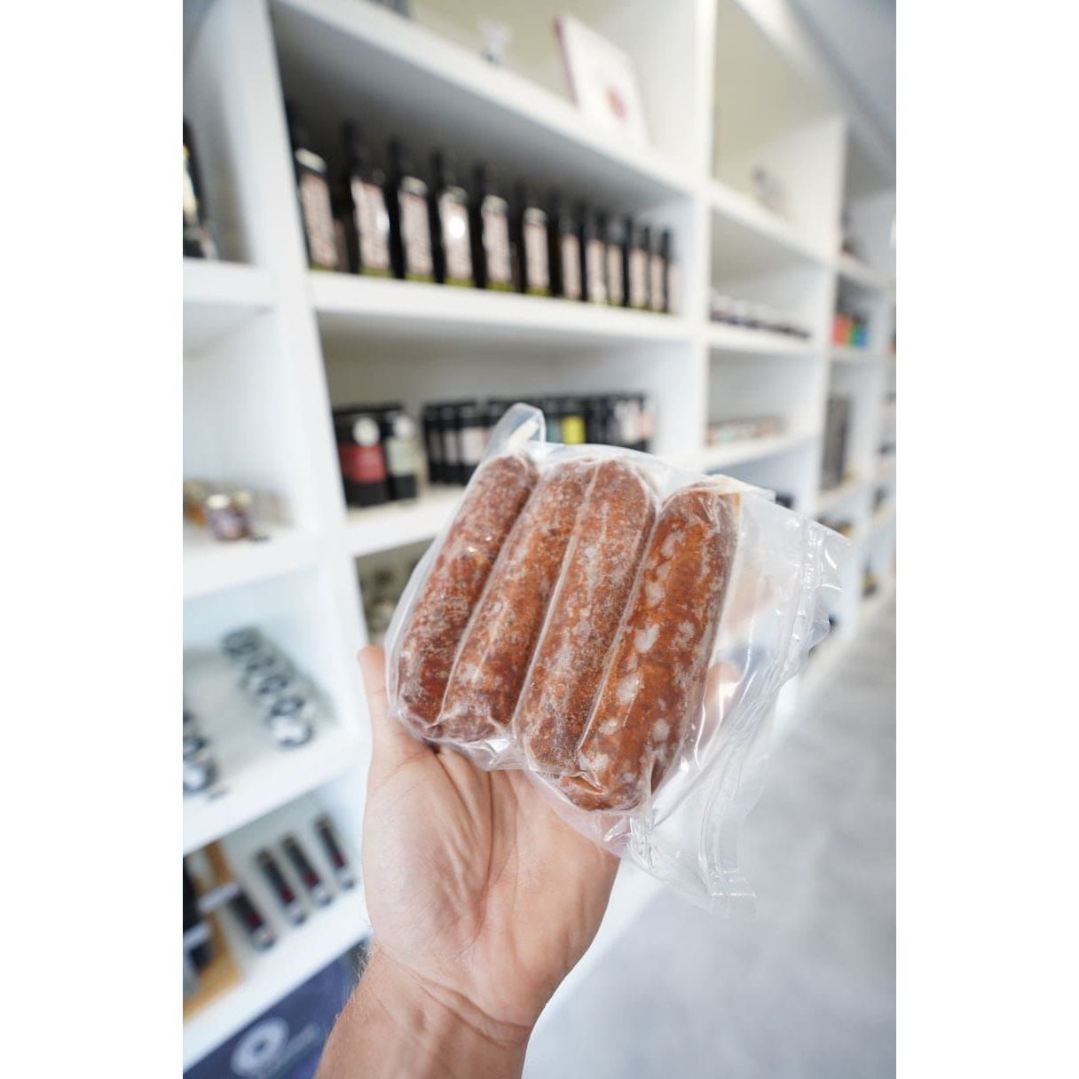 Hand holding a vacuum-sealed package of frozen kosher wagyu beef sausages at Chu's Meat Market.