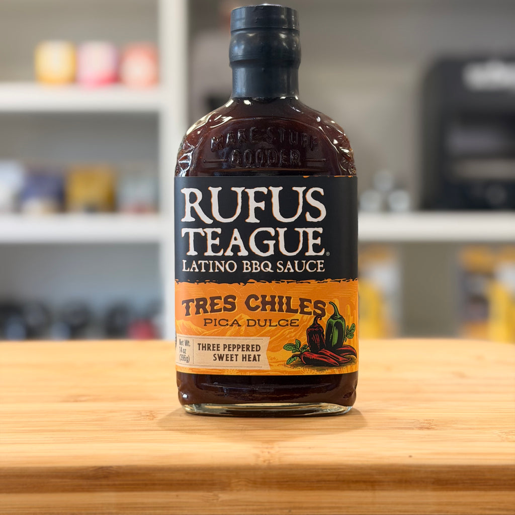 Bottle of Rufus Teague Latino BBQ Sauce on a wooden surface with a blurred kitchen background