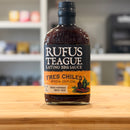Bottle of Rufus Teague Latino BBQ Sauce on a wooden surface with a blurred kitchen background