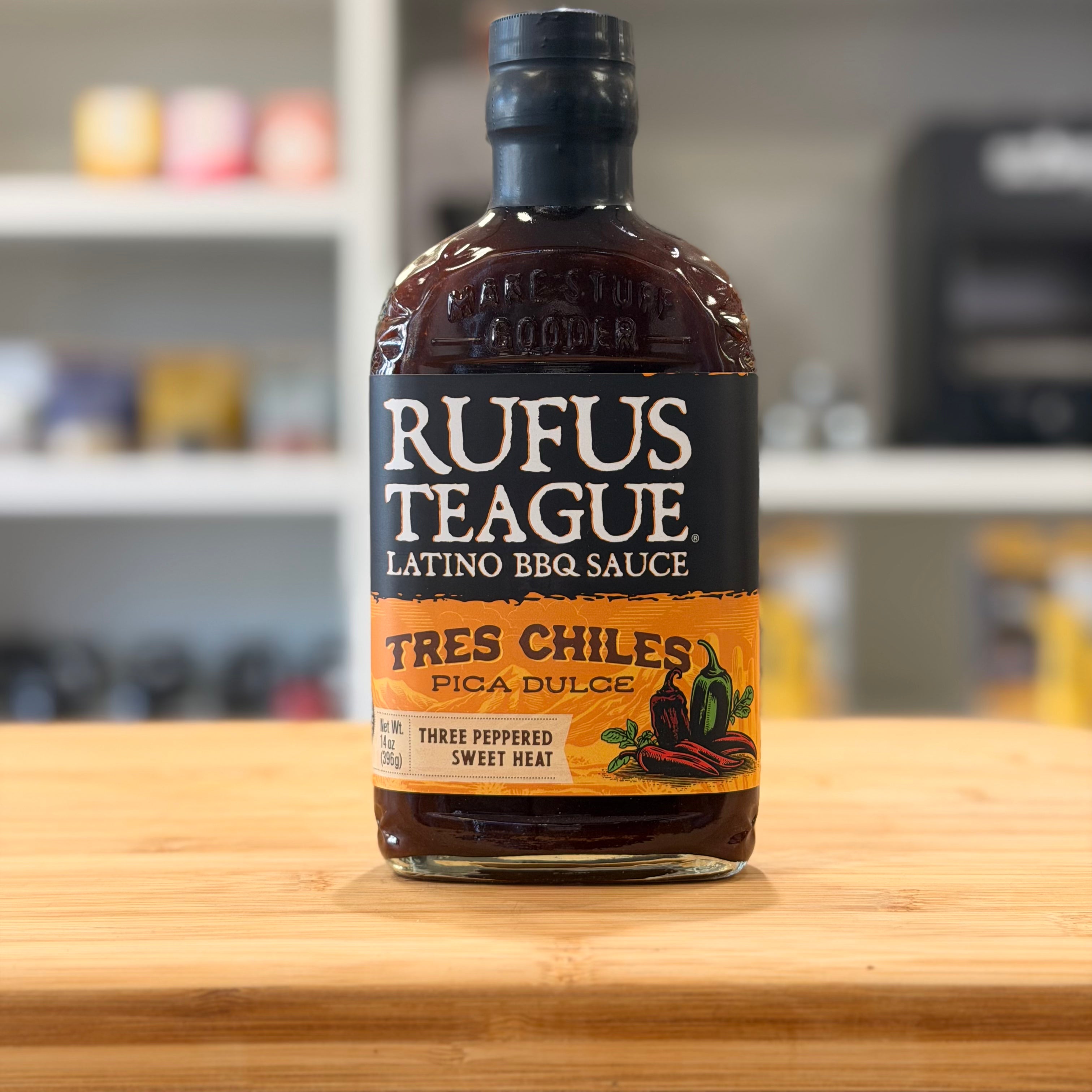 Bottle of Rufus Teague Latino BBQ Sauce on a wooden surface with a blurred kitchen background