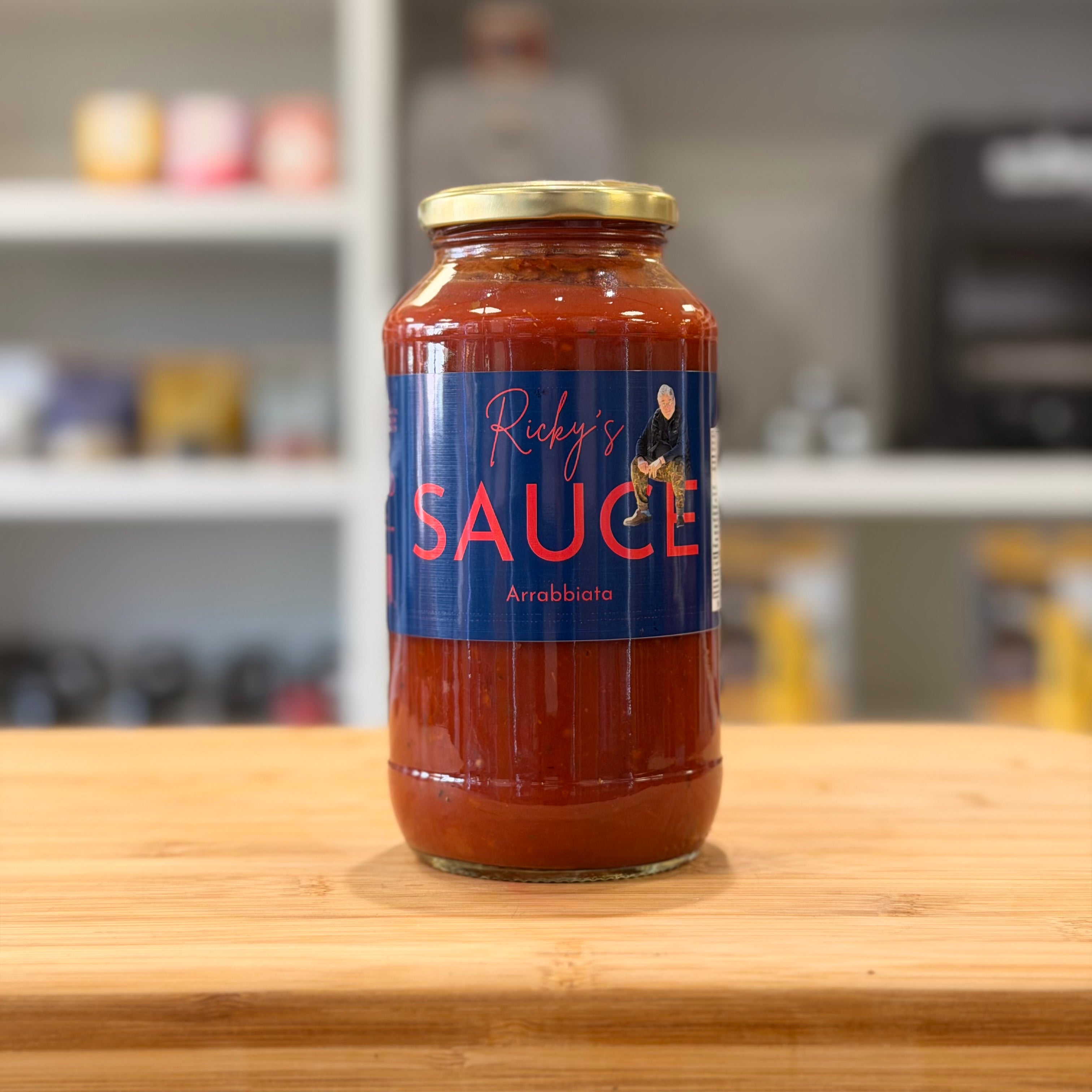 Jar of 'Ricky's Sauce' on a wooden surface with a blurred kitchen background