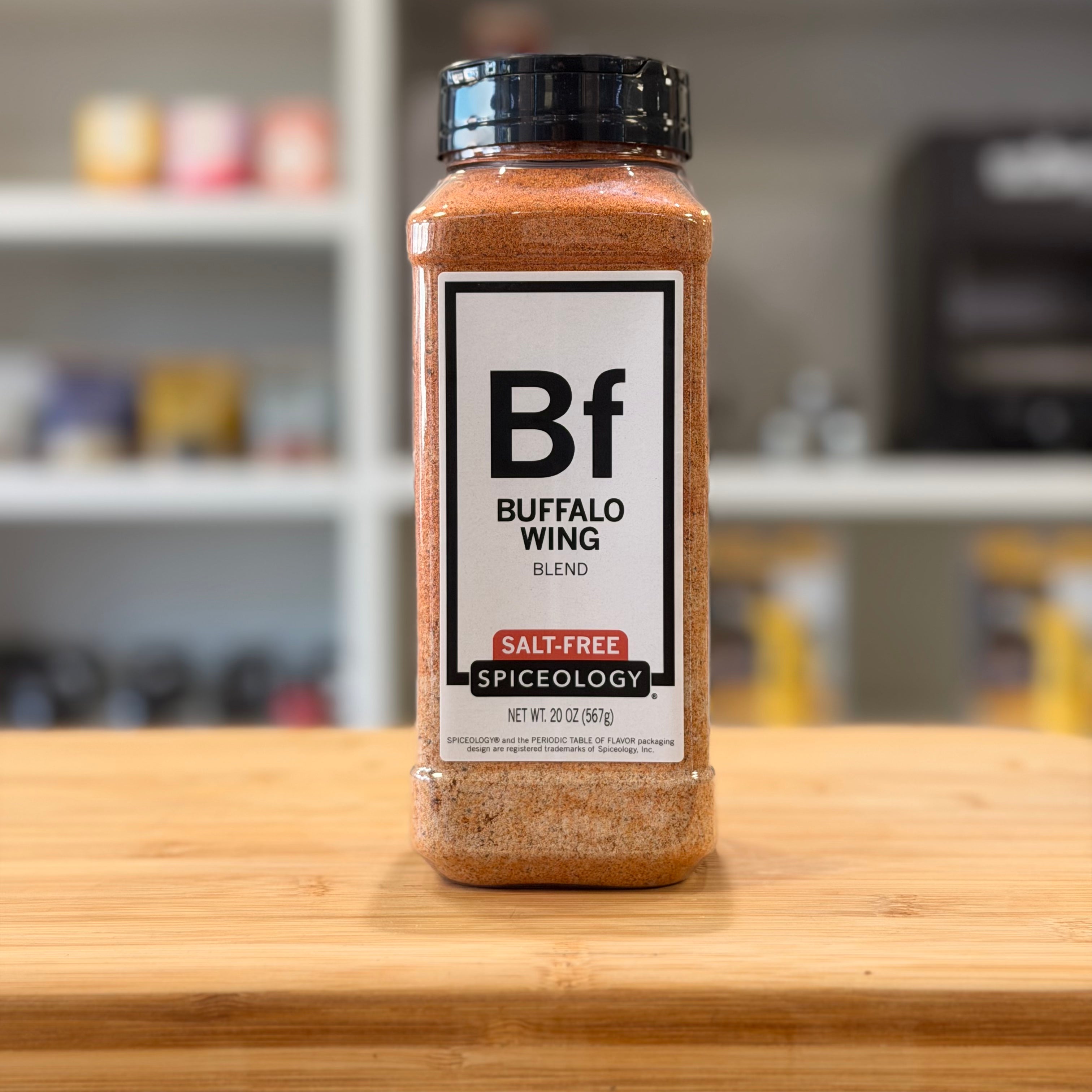 Spiceology Buffalo Wing Blend spice jar on a wooden surface with a blurred kitchen background