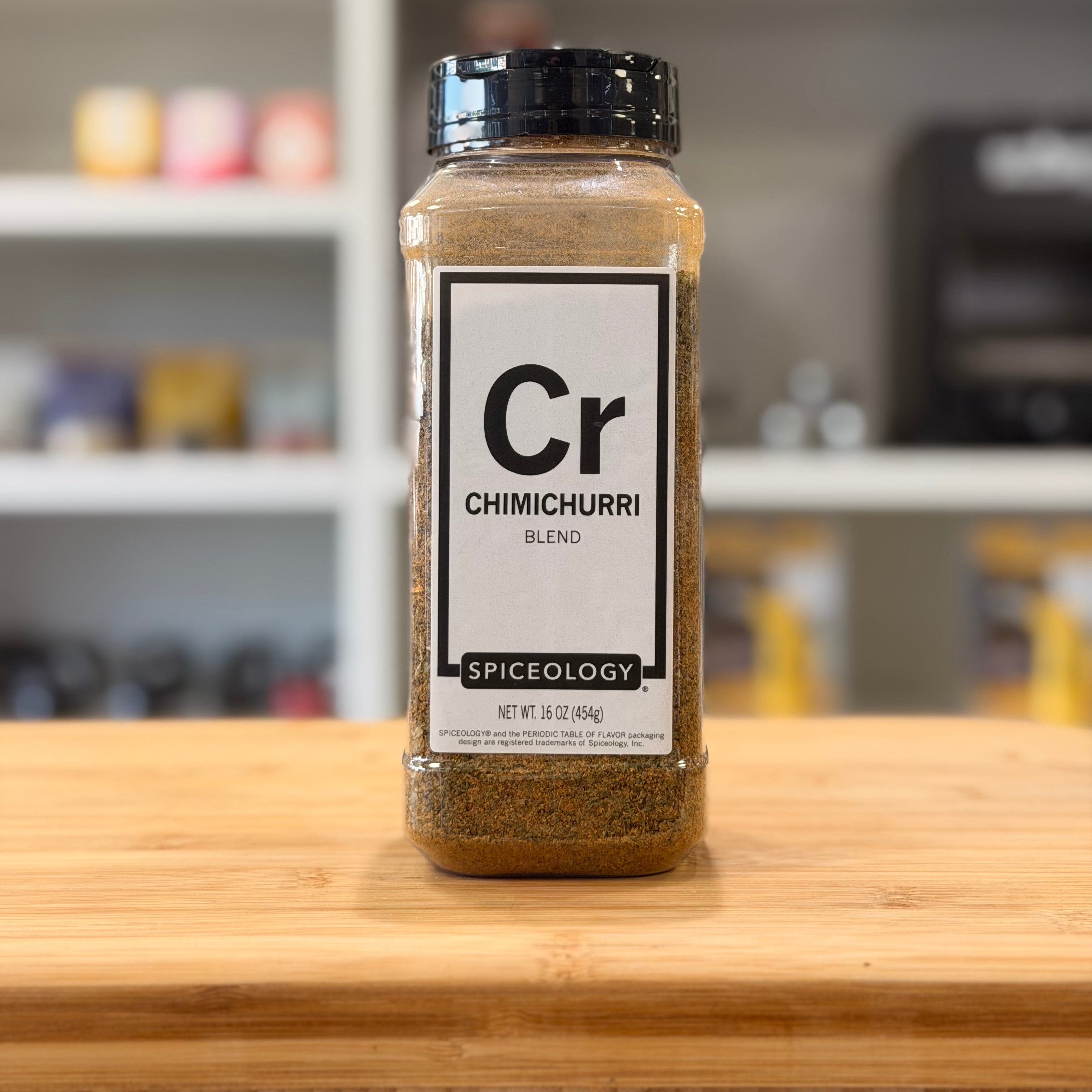 Spiceology Chimichurri blend spice jar on a wooden surface with a blurred kitchen background