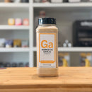 Bottle of Domestic Garlic Granules by Spiceology on a wooden surface with a blurred kitchen background.