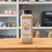 Bottle of Domestic Garlic Granules by Spiceology on a wooden surface with a blurred kitchen background.