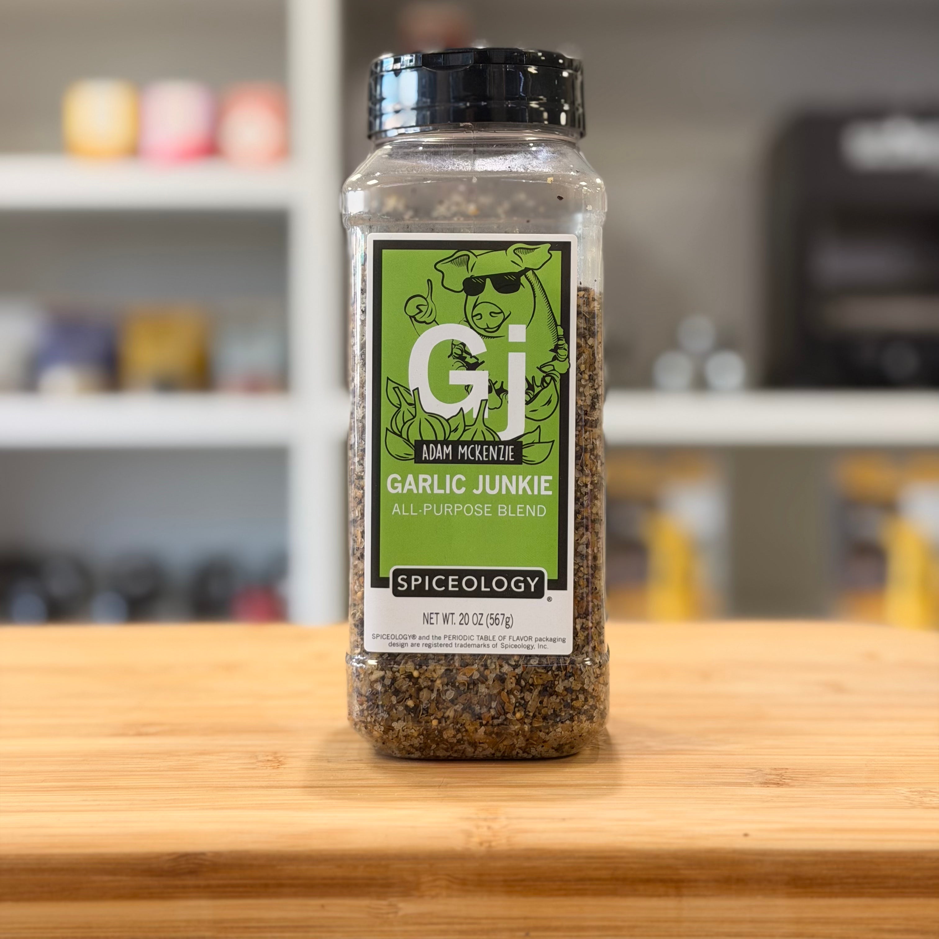 Spice bottle labeled 'Garlic Junkie' by Spiceology on a wooden surface with a blurred kitchen background.