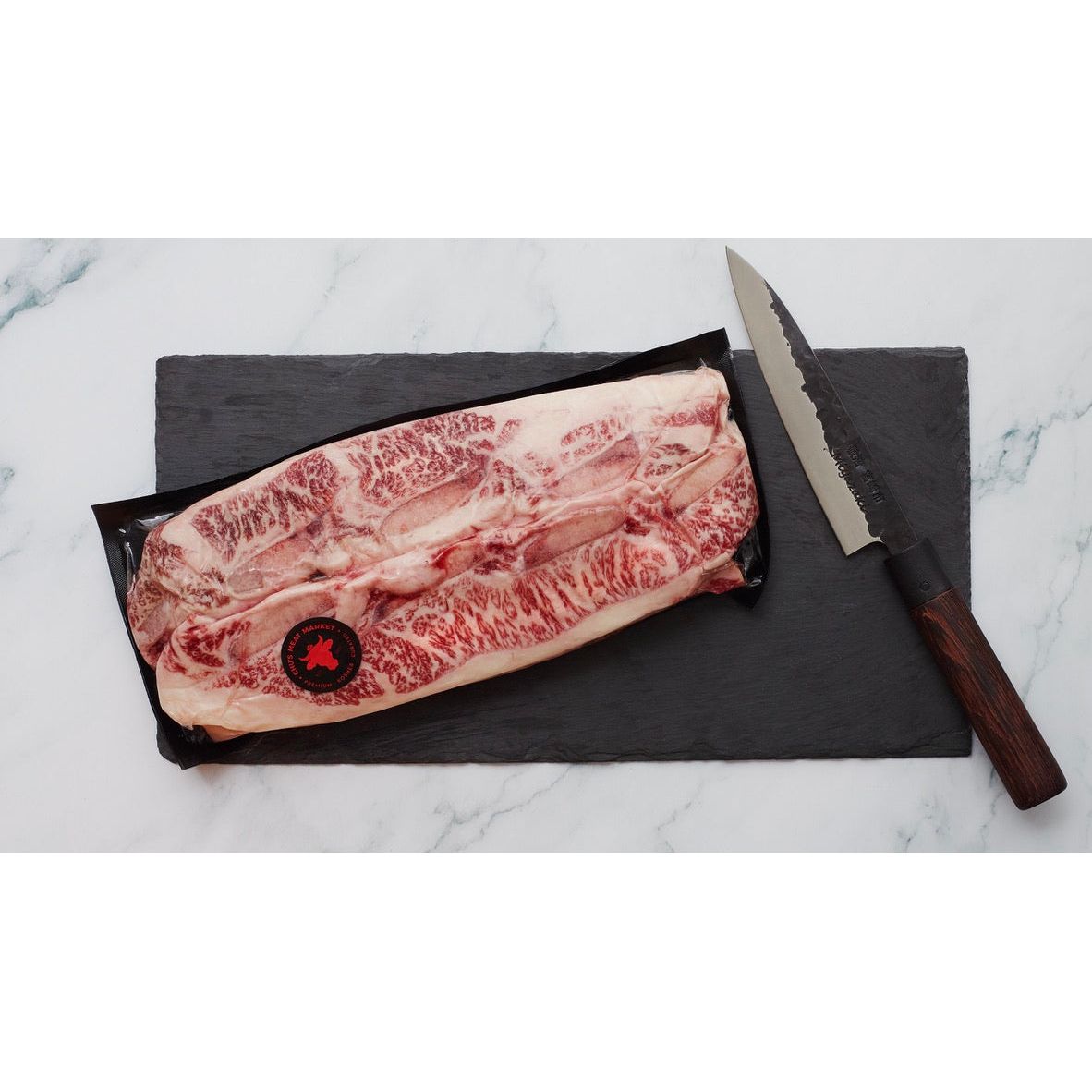 Raw marbled beef on a black slate board with a knife on a marble surface