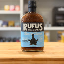 Bottle of Rufus Teague Slim N' Sweet sauce on a wooden surface with a blurred background