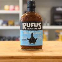 Bottle of Rufus Teague Slim N' Sweet sauce on a wooden surface with a blurred background