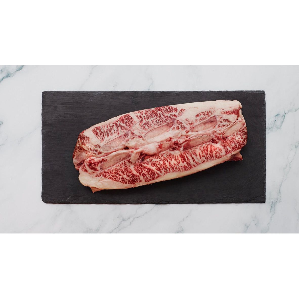 Marbled raw beef on a black slate board with a marble background