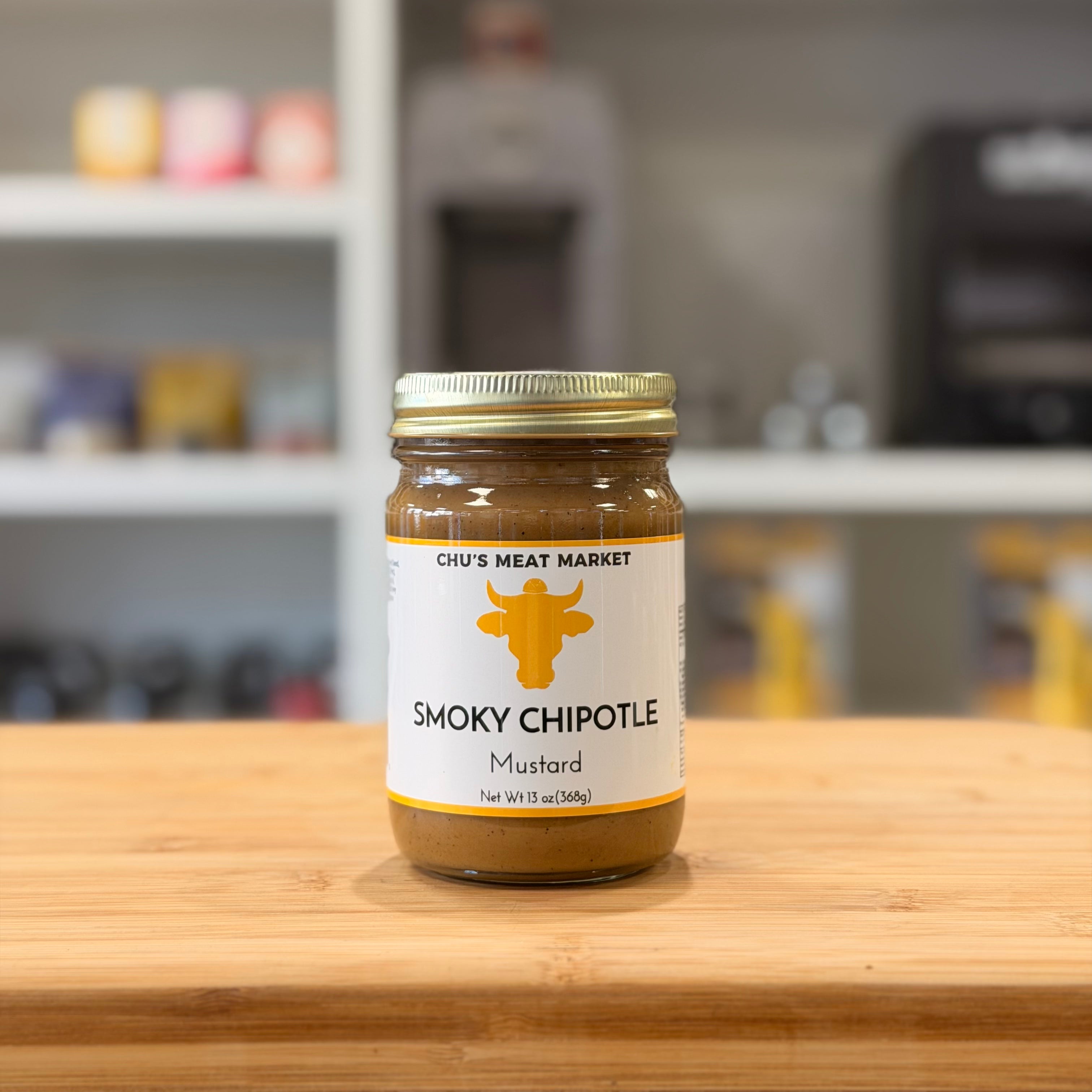 Jar of Chu's Meat Market Smoky Chipotle Mustard on a wooden surface with a blurred background