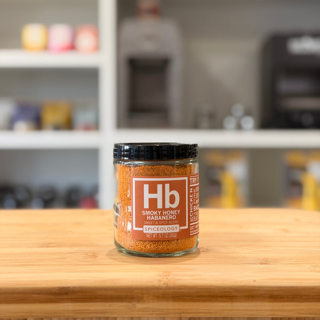 Jar of Hb Smoky Honey Habanero spice on a wooden surface with a blurred kitchen background