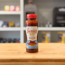 Suzie's Hot Organic Sauce bottle on a wooden surface with a blurred kitchen background