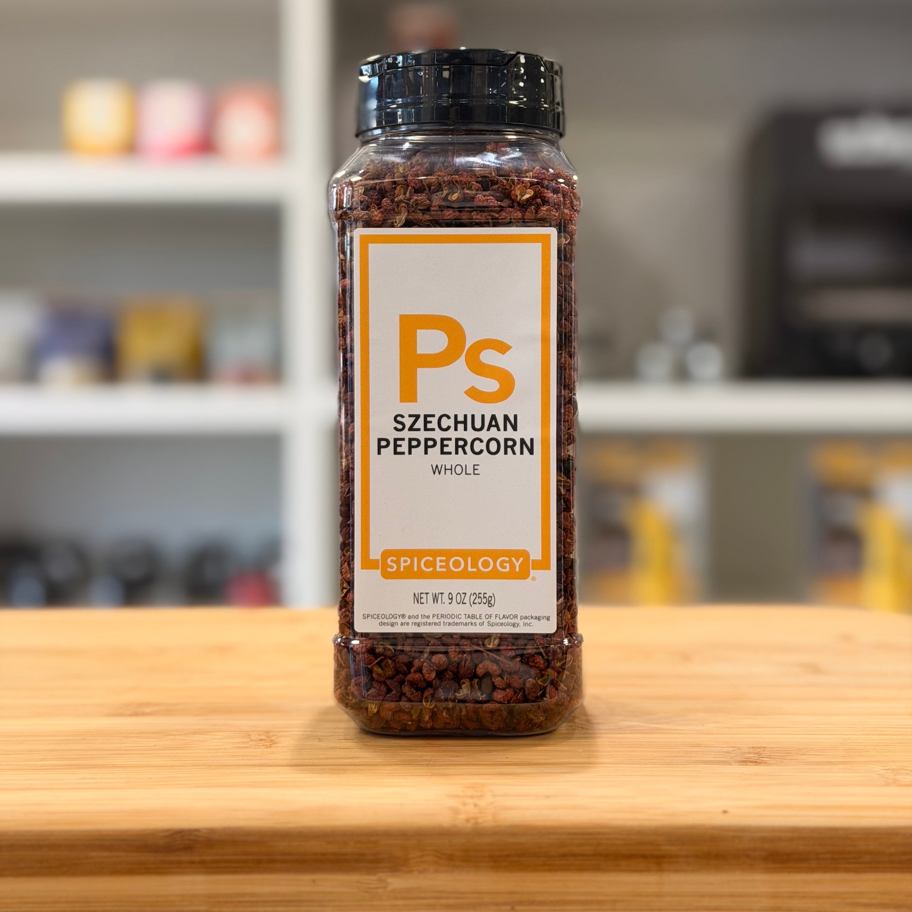 Bottle of Szechuan peppercorn on a wooden surface with a blurred kitchen background