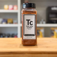 Spiceology Thai Red Curry blend jar on a wooden surface with a blurred kitchen background