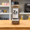 Spiceology Za'atar spice blend jar on a wooden surface with a blurred kitchen background