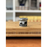 Small jar of black truffle salt on a wooden surface with a blurred background
